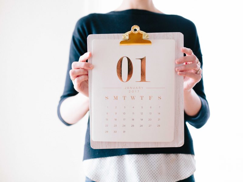 A person holding a calendar up in front of them. A large zero one is displayed on the page with the days of the week listed below.